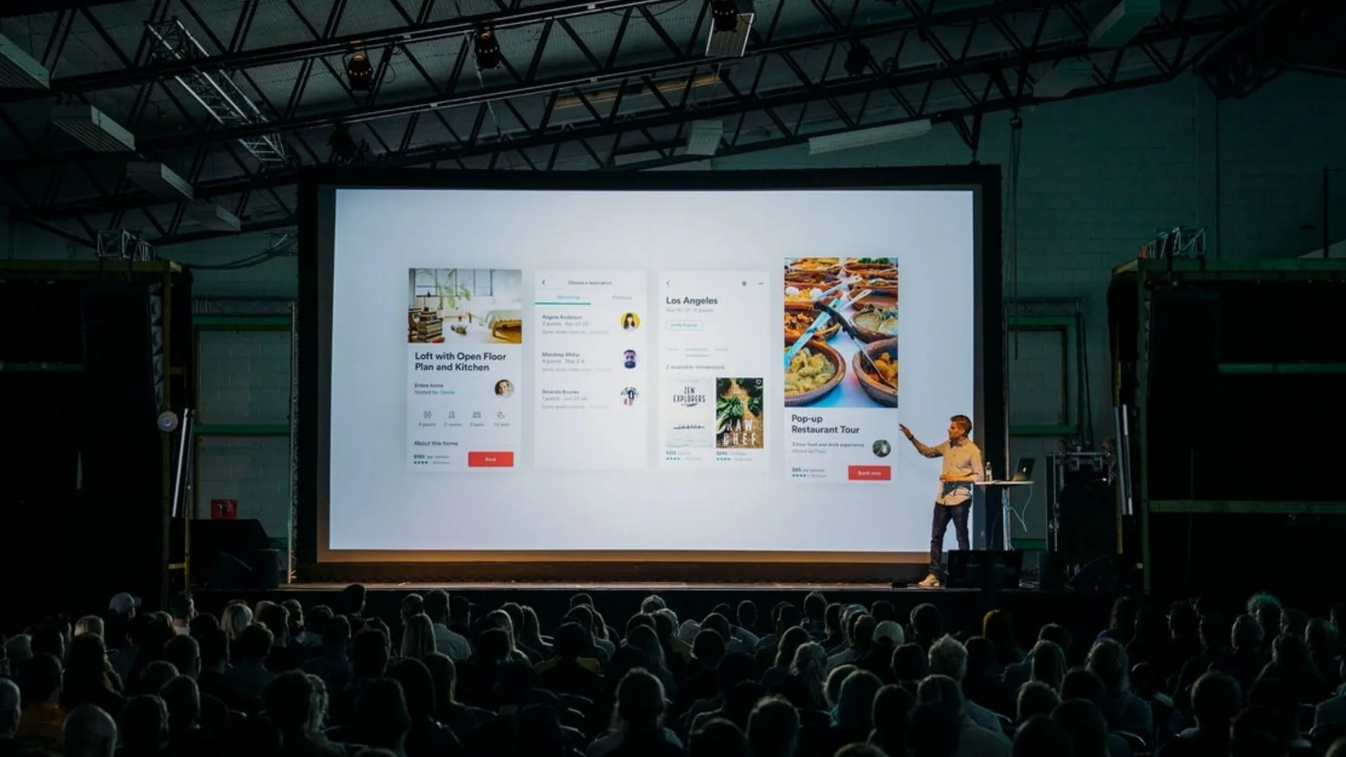 Speaker presenting app design slides on a large screen to an audience in a dark auditorium