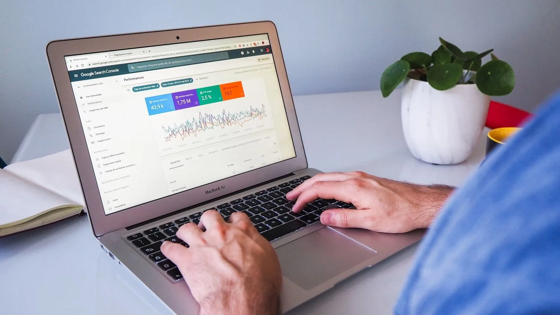 Person typing on a MacBook Air showing a Google Search Console performance report, with a potted plant beside it
