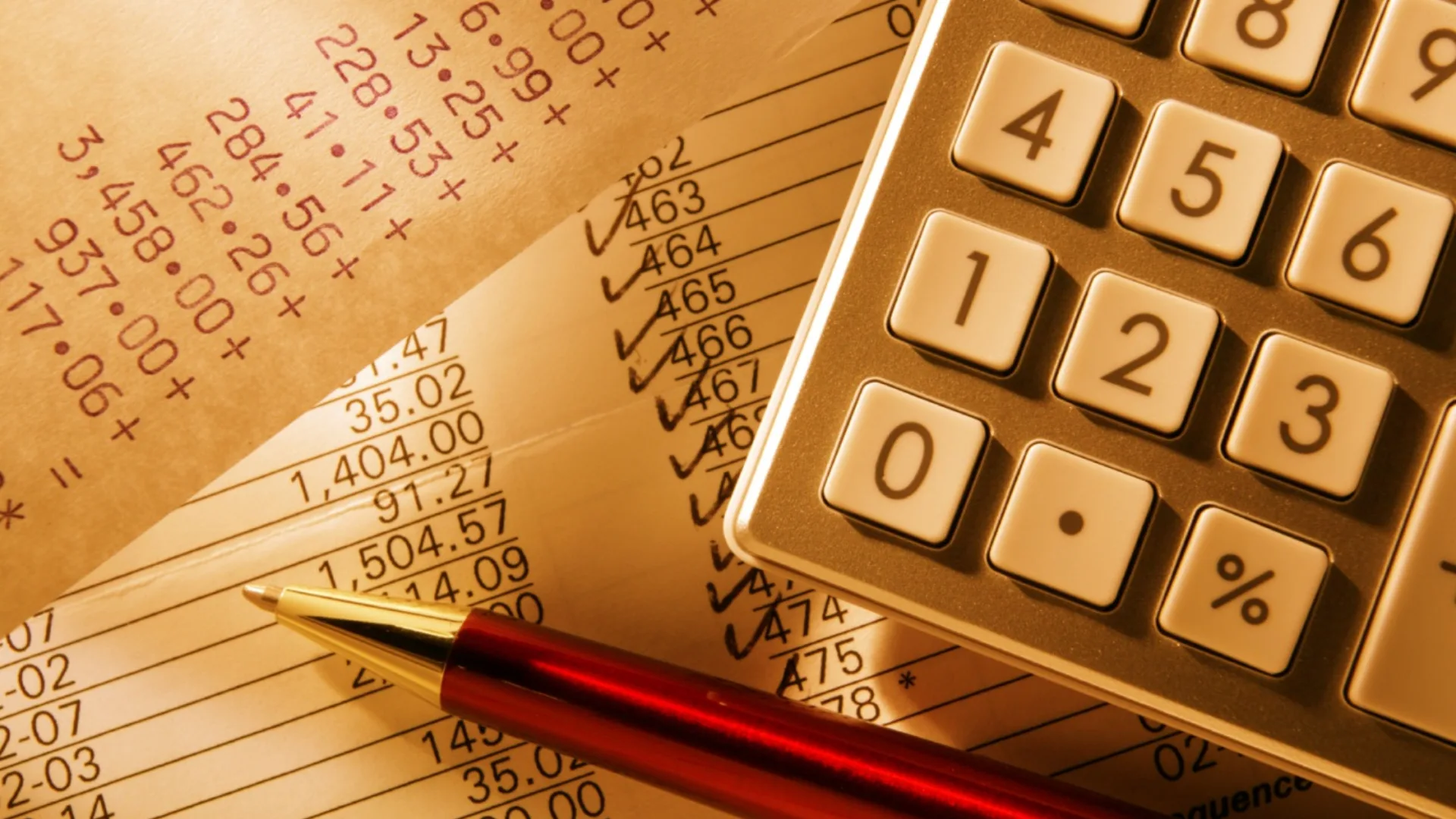 Calculator keypad, a red pen and printed financial figures with ticked entries